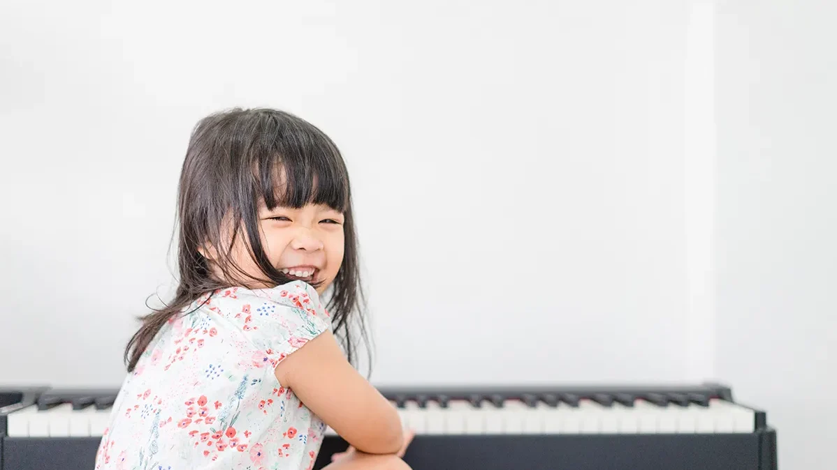 ピアノの前で笑顔でこちらを見る女の子